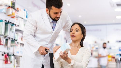 Preparar un viaje accesible: Usuario de silla de ruedas preguntando a un farmacéutico por un medicamento.