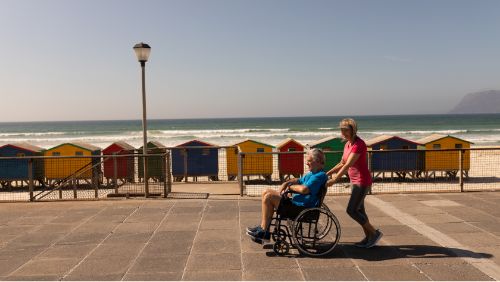Atracciones de Mallorca: Mujer y marido en silla de ruedas paseando por un paseo marítimo.